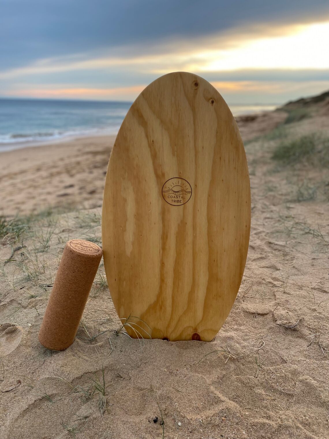 Wooden Surf Balance Board made by Coastal Tribe sitting vertically in the sand at the beach