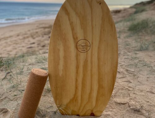 Wooden Surf Balance Board made by Coastal Tribe sitting vertically in the sand at the beach