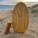 Wooden Surf Balance Board made by Coastal Tribe sitting vertically in the sand at the beach